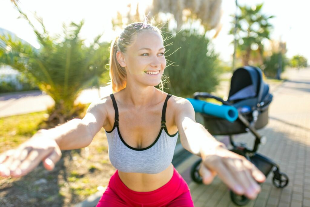 blonde yound mom working out outdoors warming up with yoga mat in tropical beach