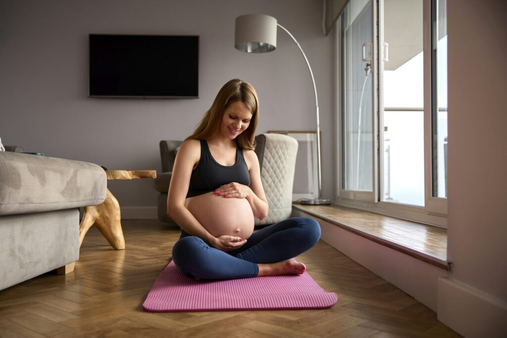 Pregnant Woman Wearing Fitness Clothing On Exercise Mat At Home Doing Yoga