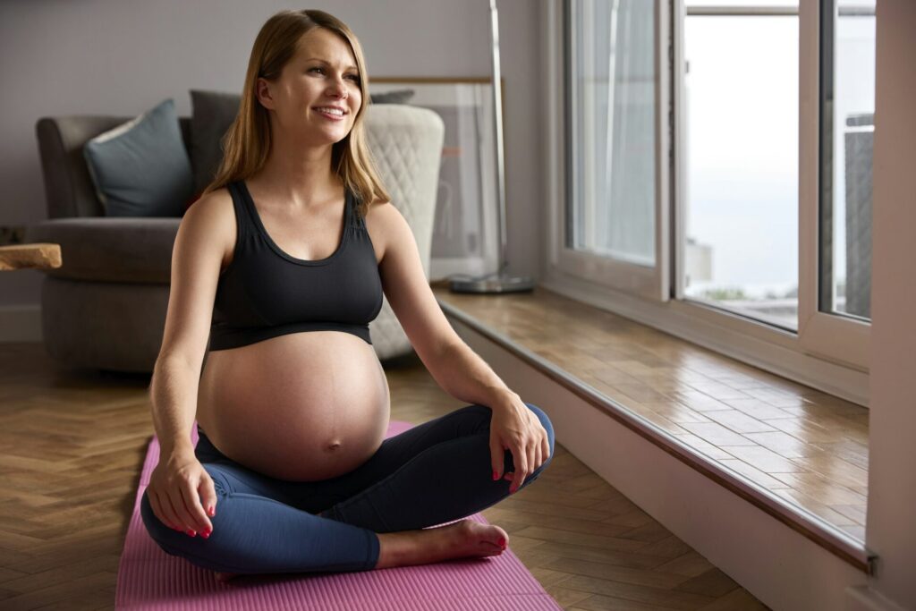 Pregnant Woman Wearing Fitness Clothing On Exercise Mat At Home Doing Yoga